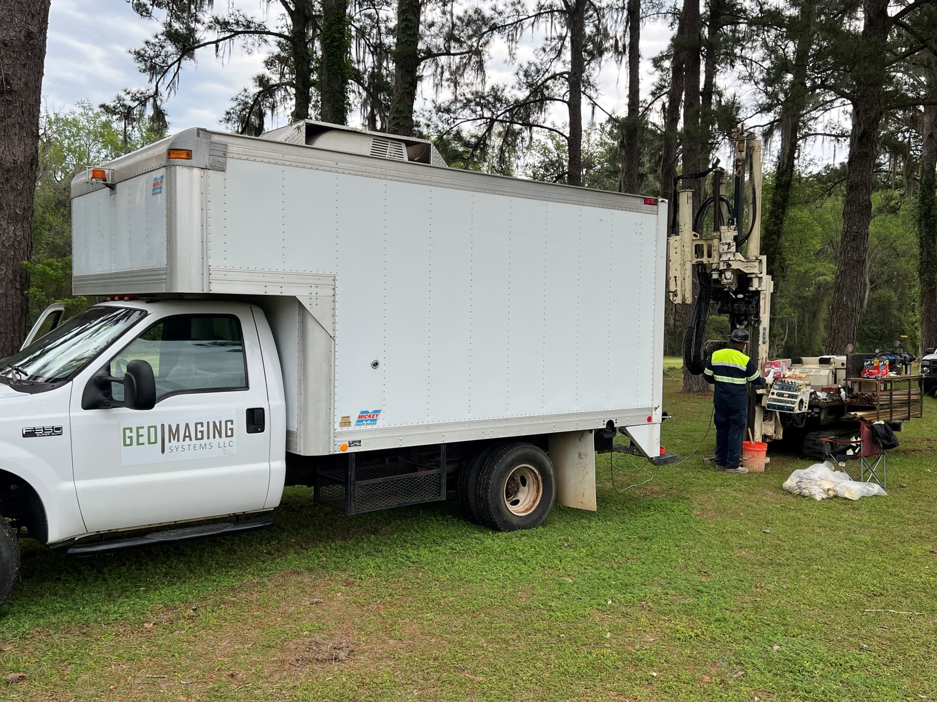 The GeoImaging equipment truck parked on grass at a wooded site with a direct-push rig working beside it