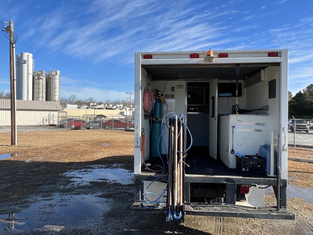 The GeoImaging data acquisition truck parked with its rear doors open, showing the bench workstation, gas cylinders, hose reels and drive rods stowed inside