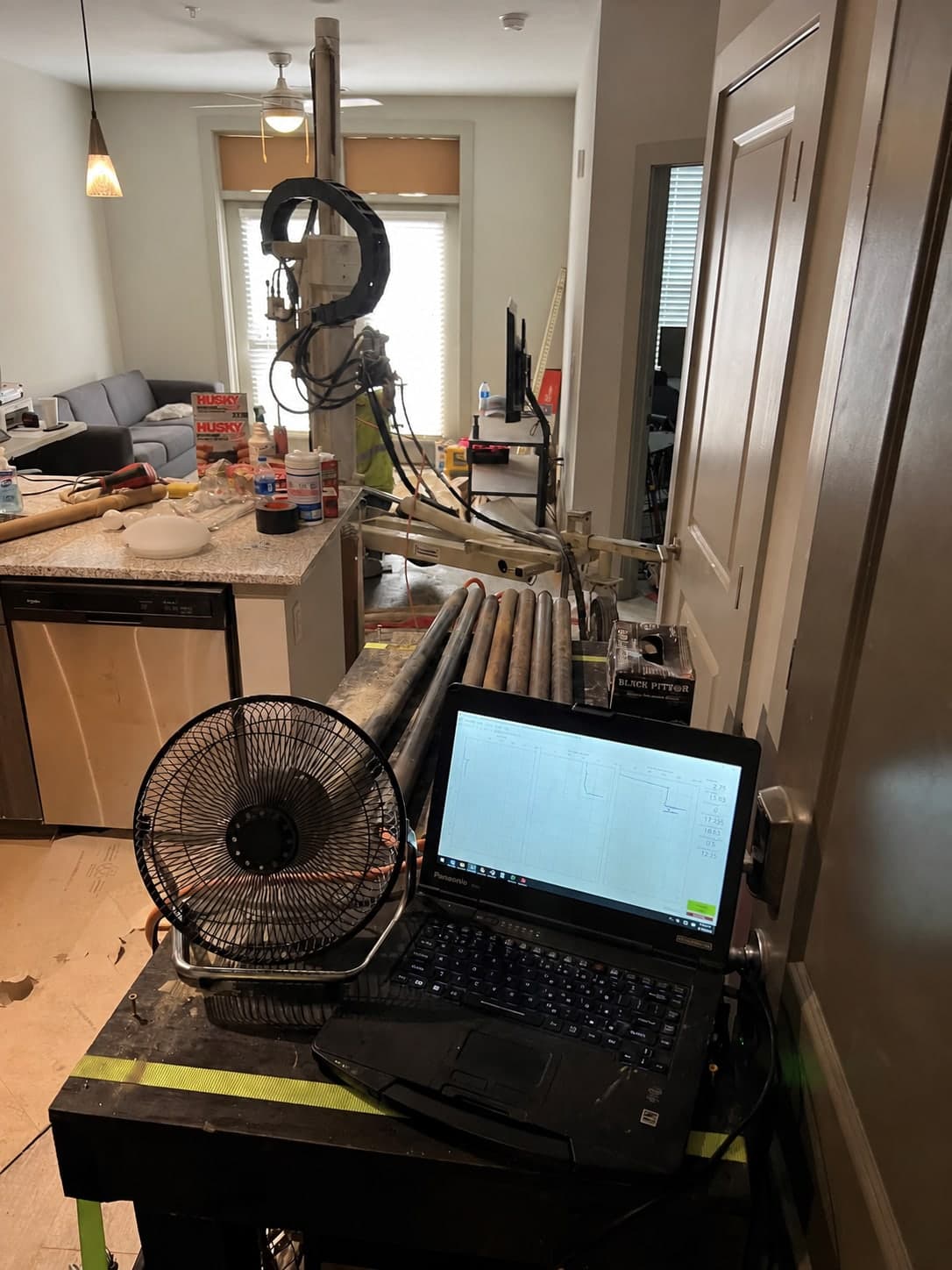 A compact direct-push platform set up inside a finished residential interior, its mast reaching the ceiling, with the logging laptop running on a table beside it
